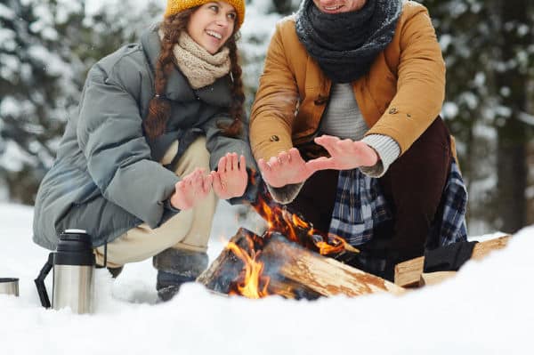Travelers warming hands by winter campfire