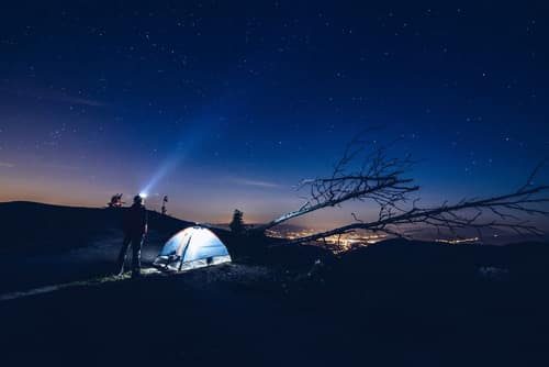 man standing outside a tent with head torch