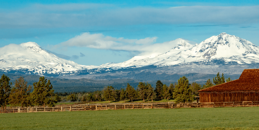 A panoramic image of the snow covered three sisters mountains with a barn and pasture in foreground, near Bend, Oregon