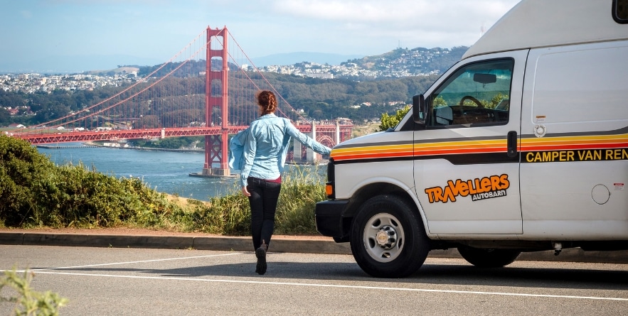 Person standing next to campervan with view of the Golden Gate Bridge, USA