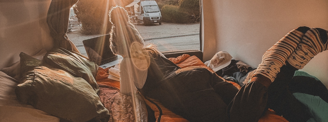person sitting in back of campervan with sleeping bag